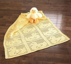 a yellow crocheted blanket on the floor with a stuffed duck sitting on it