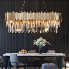 a chandelier hanging over a dining table with chairs and vases on it