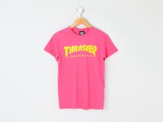 This vintage 2000s t-shirt has sharp graphics. The tag size is S - it measures 18" across the chest laid flat, and it measures 26" long shoulder-to-hem. This item is in excellent vintage condition.   Tag information:  - 100% cotton - Machine wash cold. Tumble dry low. - Originally by Thrasher Size and fit:  - Tag size is S   - Chest: 18" across    - Length: 26" long shoulder-to-hem 90s Style Pink T-shirt With Graphic Print, Pink Y2k T-shirt For Streetwear, Pink Urban T-shirt For Streetwear, 90s Letter Print T-shirt For Skateboarding, 90s Skateboarding Letter Print T-shirt, 90s Style Pink T-shirt With Letter Print, Pink Graffiti Print T-shirt For Streetwear, 90s Pink T-shirt For Streetwear, Retro Pink T-shirt For Streetwear