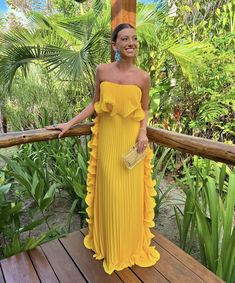 a woman in a yellow dress standing on a wooden deck with palm trees behind her