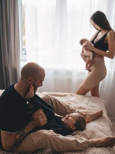 a man and woman sitting on top of a bed next to a baby in a sling