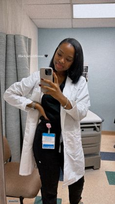 a woman is taking a selfie in the mirror with her cell phone while wearing black pants and a white lab coat