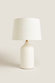 a white table lamp with a beige shade on the base and a light bulb attached to it