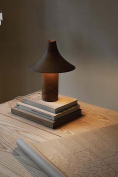 a lamp sitting on top of a wooden table next to two books and a pen