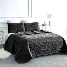 a bed in a white room with black comforter and pillows on top of it