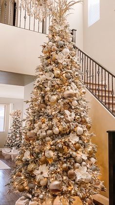 a decorated christmas tree in the middle of a room with stairs and chandelier