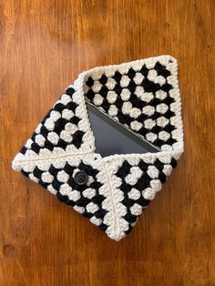 a black and white crocheted case sitting on top of a wooden table next to a cell phone