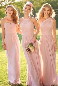 three bridesmaids in pink dresses posing for a photo together on the lawn at their wedding