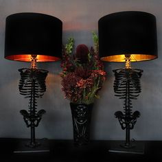 two skeleton lamps are next to a vase with flowers in it on a black table