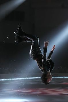 a man doing a handstand on his skateboard in front of a spotlight