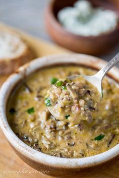 a spoon full of soup sitting on top of a wooden cutting board next to bread