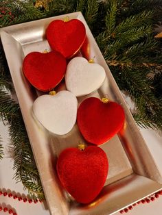 four red and white heart shaped cookies on a silver tray with pine branches in the background