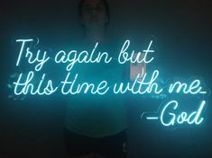 a woman standing in front of a neon sign that reads try again but this time with me god