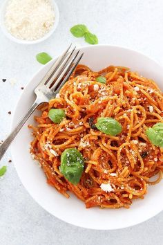 a white bowl filled with pasta and sauce on top of a table next to a fork