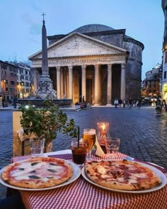 two pizzas sitting on top of a table in front of a building with columns