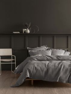 a bed sitting in a bedroom next to a white chair and wooden floored wall