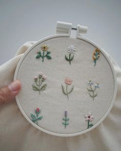 a hand is holding up a white embroidery hoop with small flowers on it, and the bottom half of the hoop has been stitched together