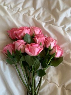 a bunch of pink roses sitting on top of a white sheet covered bed with green leaves