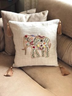 an embroidered elephant pillow on a couch with tassels