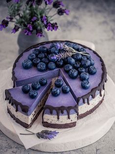 a cake with blueberries on top is sitting on a table next to purple flowers