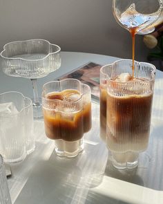 two glasses filled with liquid sitting on top of a table next to another set of glasses