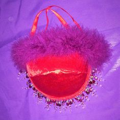 a red purse with purple fur and beads on it's side sitting on a purple surface