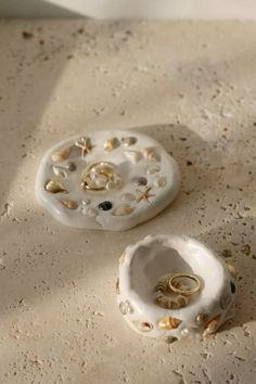 two rings sitting on top of a white ceramic container with shells and seashells