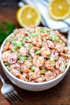 a white bowl filled with shrimp salad next to a fork and lemon wedges on the side