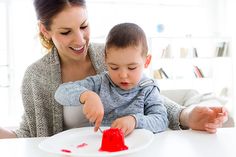 a woman is playing with a child's paint on a white plate at the table