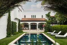 the pool is surrounded by lush green plants and lawn chairs, with an outdoor patio in the background