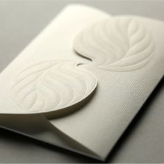 a white business card with a leaf design on the front and back side, sitting on top of a gray surface