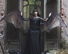 a woman dressed in black stands outside an old building with her wings spread wide open