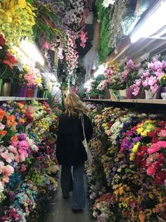 a woman walking through a flower shop filled with lots of flowers