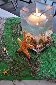 a starfish and sea shells in a glass container on a green table cloth with a lit candle