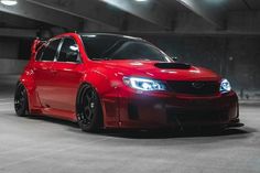 a red car is parked in an empty parking garage with its hood up and lights on