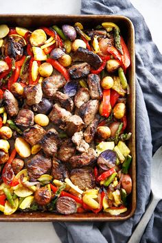 a pan filled with meat and vegetables on top of a blue cloth next to a fork