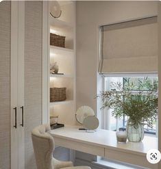 a white desk sitting under a window next to a vase with a plant in it