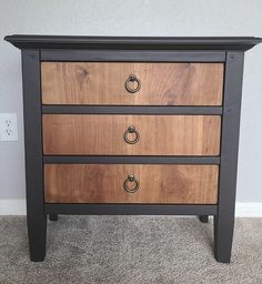 a black and brown dresser with three drawers on it's sides, in front of a white wall