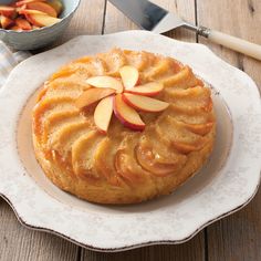 a cake with apples on top sitting on a plate next to a bowl of fruit