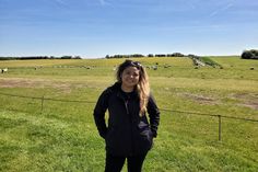 a woman standing in front of a fence on top of a lush green field filled with animals