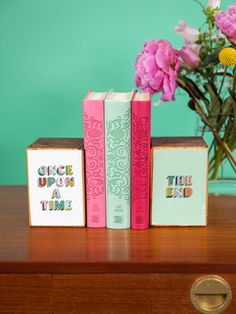 three books sitting on top of a wooden table next to a vase with pink flowers