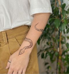 a woman with a snake tattoo on her left arm and right hand is wearing brown pants