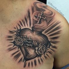 a cross and heart tattoo on the back of a man's shoulder with roses