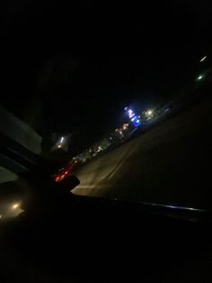 the view from inside a car at night with city lights in the distance and oncoming traffic