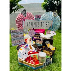 a box filled with lots of different items on top of a grass covered field next to a sign that says parents to be