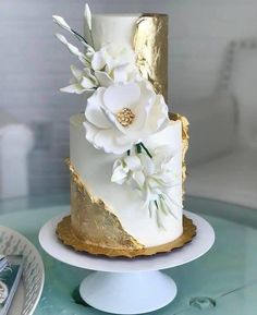 a white and gold wedding cake with flowers on top