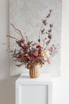 a vase filled with lots of flowers sitting on top of a white table next to a wall