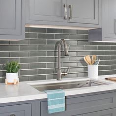 a kitchen with gray cabinets and white counter tops, silver faucet over the sink