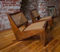 three wooden chairs sitting on top of a hard wood floor next to a brick wall