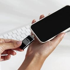 a woman is holding a cell phone in her left hand and typing on the keyboard